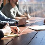 Team Business - people sitting on chair in front of table while holding pens during daytime