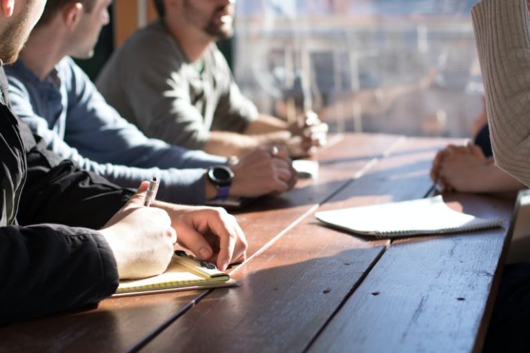 Team Business - people sitting on chair in front of table while holding pens during daytime