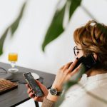 Multitasking - Busy female talking on smartphone and checking messages during work in contemporary office
