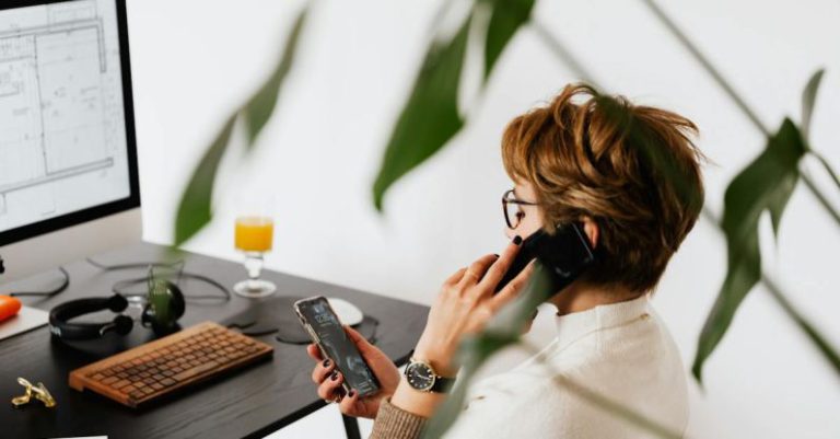 Multitasking - Busy female talking on smartphone and checking messages during work in contemporary office