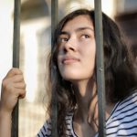 Opportunities - Sad isolated young woman looking away through fence with hope