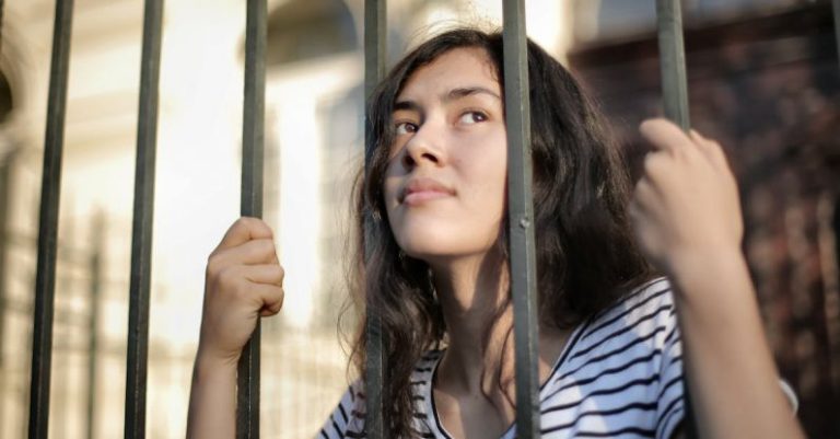 Opportunities - Sad isolated young woman looking away through fence with hope