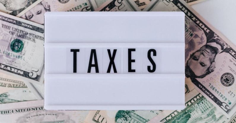 Taxes - Top view of white vintage light box with TAXES inscription placed on stack of USA dollar bills on white surface