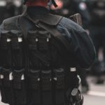 Enforcement - Back view of armed police officer wearing uniform with helmet and body armor performing duties while standing on road