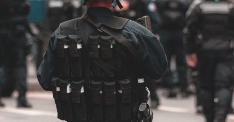 Enforcement - Back view of armed police officer wearing uniform with helmet and body armor performing duties while standing on road